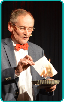 Zauberer Michael Sondermeyer Zauberer Michael Sondermeyer ist bei seinem Auftritt zu sehen und hält gerade ein brennendes Stückpapier in seiner Hand.